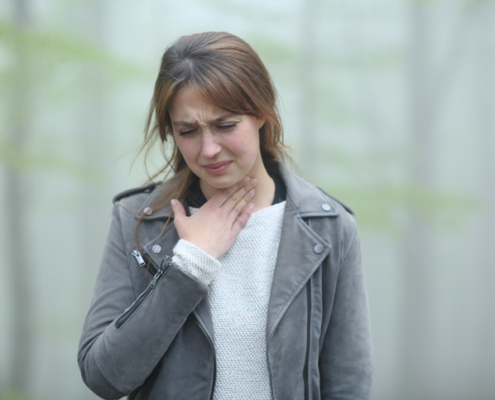 An image of a woman rubbing her sore throat in a foggy forest.